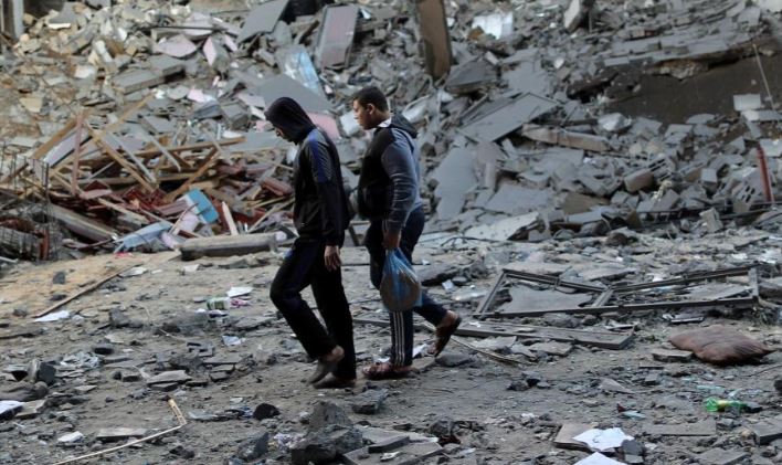 Palestinians walk past the remains of the building