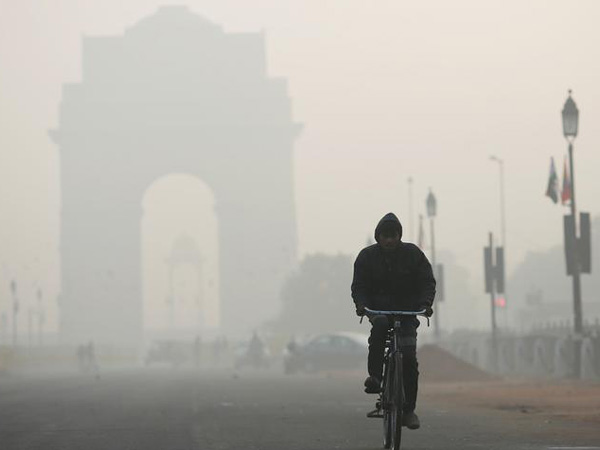 A man rides his bicycle in front of the India Gate shrouded in smog in New Delhi