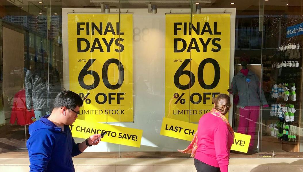 Shoppers walk past sales signs on display in the window