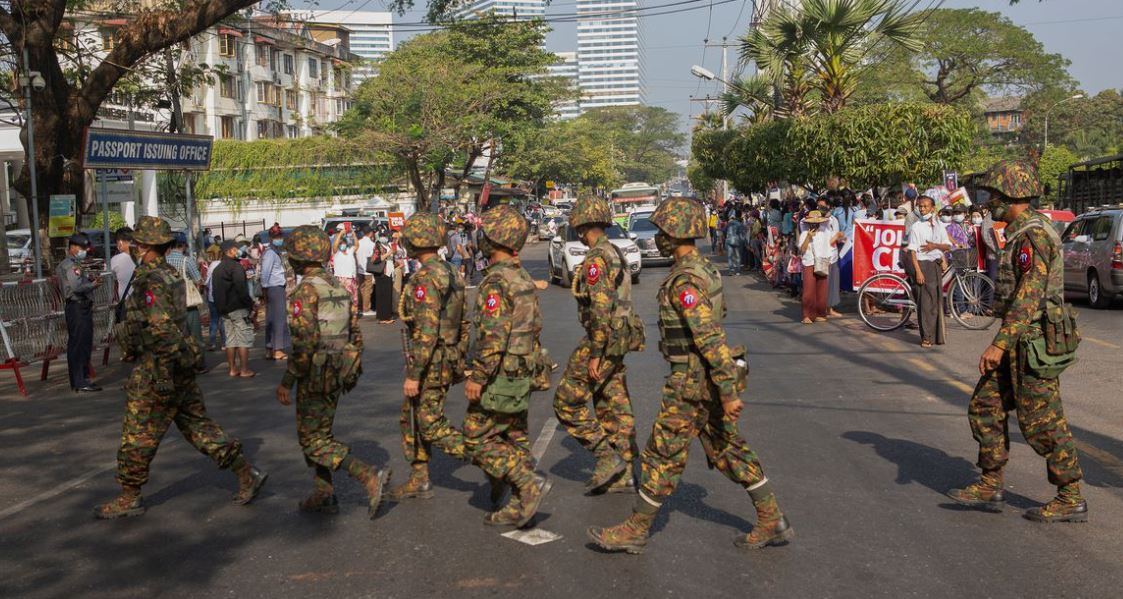 Soldiers cross a street as people gather to protest against the military coup, in Yangon