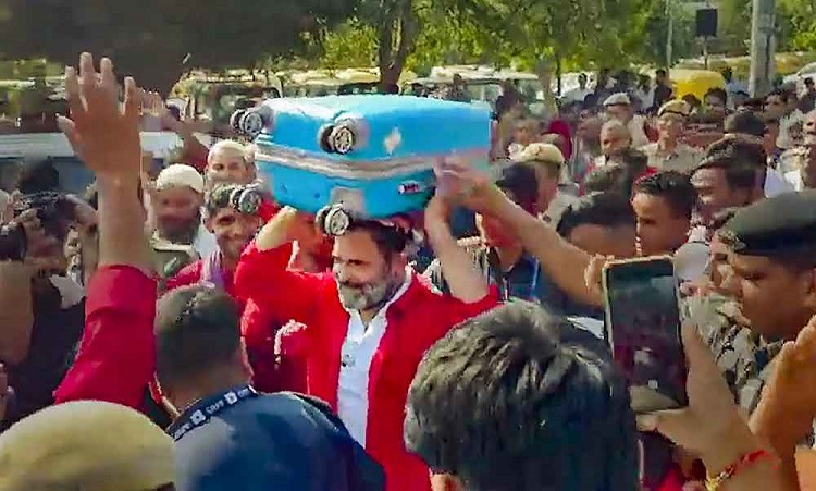 Rahul Gandhi lifts luggage over his head wearing porters' shirt